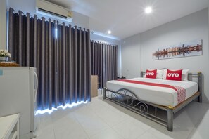 Habitación de hotel con cama, cortinas, una obra de arte de paisaje urbano y un refrigerador.