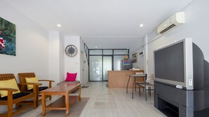 A modern living room with wooden furniture, a large flat-screen TV, and a glass door leading to a kitchen area. - OYO 75323 Tha Burapa Home Bangsean (Chonburi)