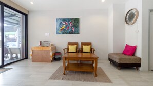 A modern living room with a wooden dining table, two chairs, a sofa, and a painting on the wall. - OYO 75323 Tha Burapa Home Bangsean (Chonburi)