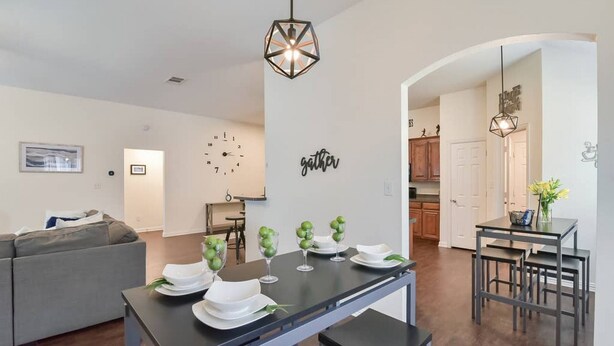 A modern living room with a dining area, featuring a sofa, a dining table set with plates and glasses, and a wall clock.
