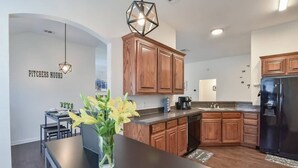 A modern kitchen with wooden cabinets, a black refrigerator, and a vase with yellow flowers on the counter.