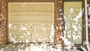 A garage door with a keypad lock, a door with a peephole, and a brick wall.