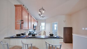 A kitchen with wooden cabinets, a central island with bar stools, a modern chandelier, and a view to the dining area.