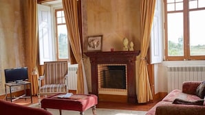 A living room with a fireplace, a television, and a striped armchair. - Hotel Rural Quinta do Juncal (Peniche)