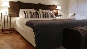 A neatly made bed with striped pillows, a dark throw blanket, and a suitcase on the floor. - Hotel Rural Quinta do Juncal (Peniche)