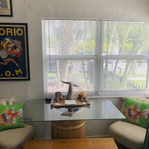 Relax in this serene room with a garden view, featuring a glass-top table, two comfortable chairs with fish-print cushions, and a wooden stool.