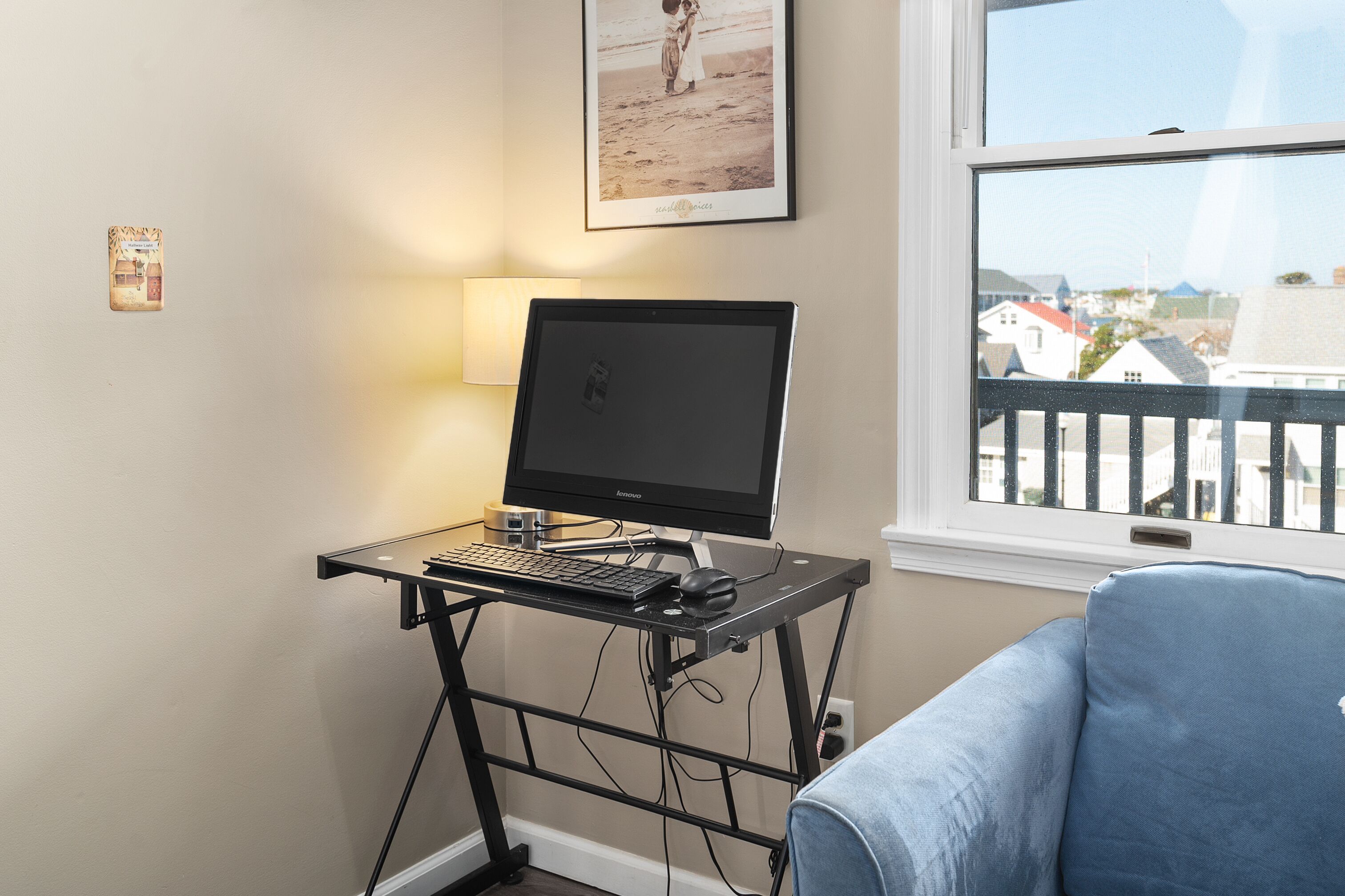 A computer desk with a monitor, keyboard, and mouse, positioned next to a window with a view of buildings.