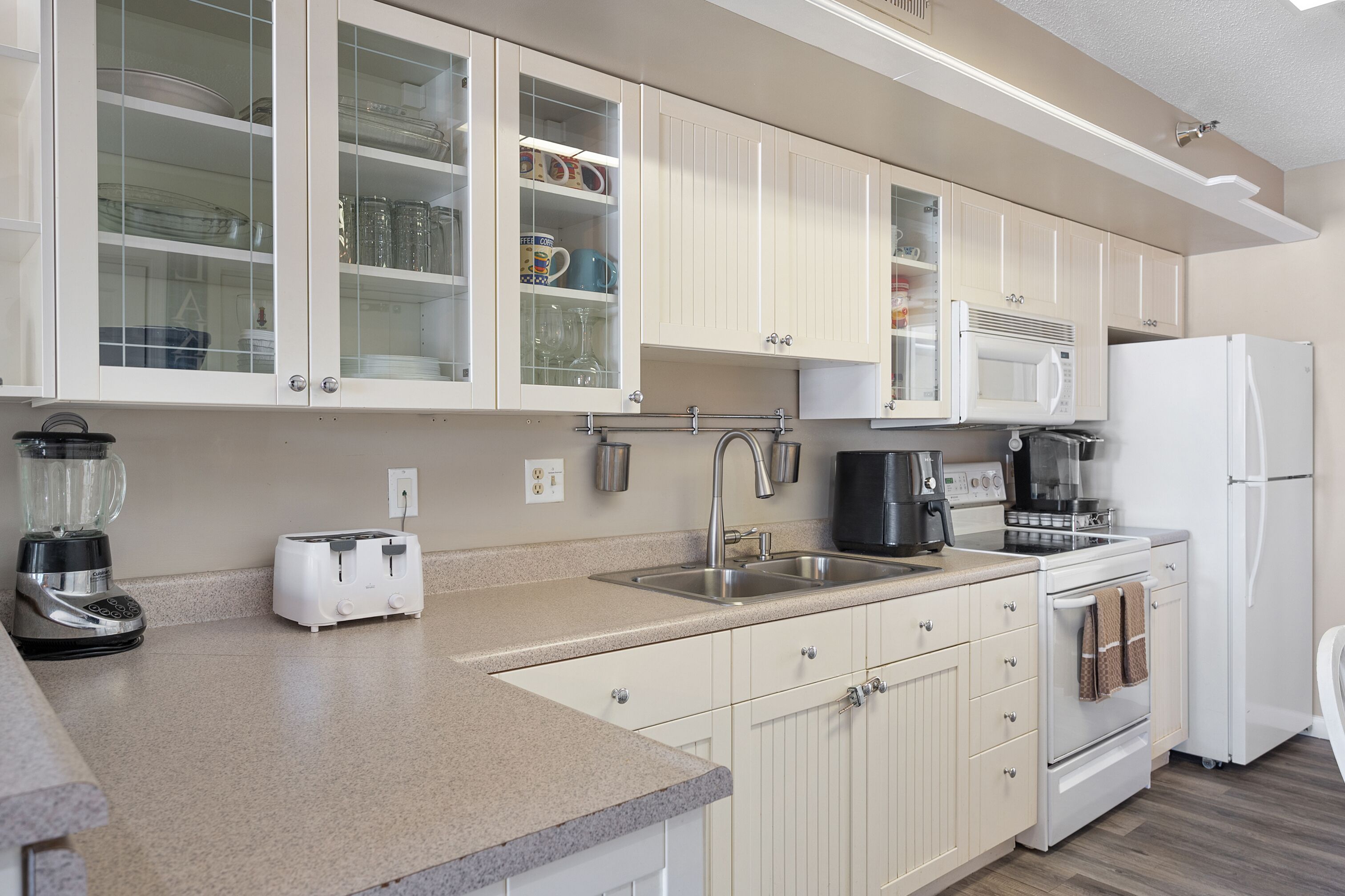 A modern kitchen with white cabinets, a built-in microwave, a refrigerator, a toaster, and a blender.