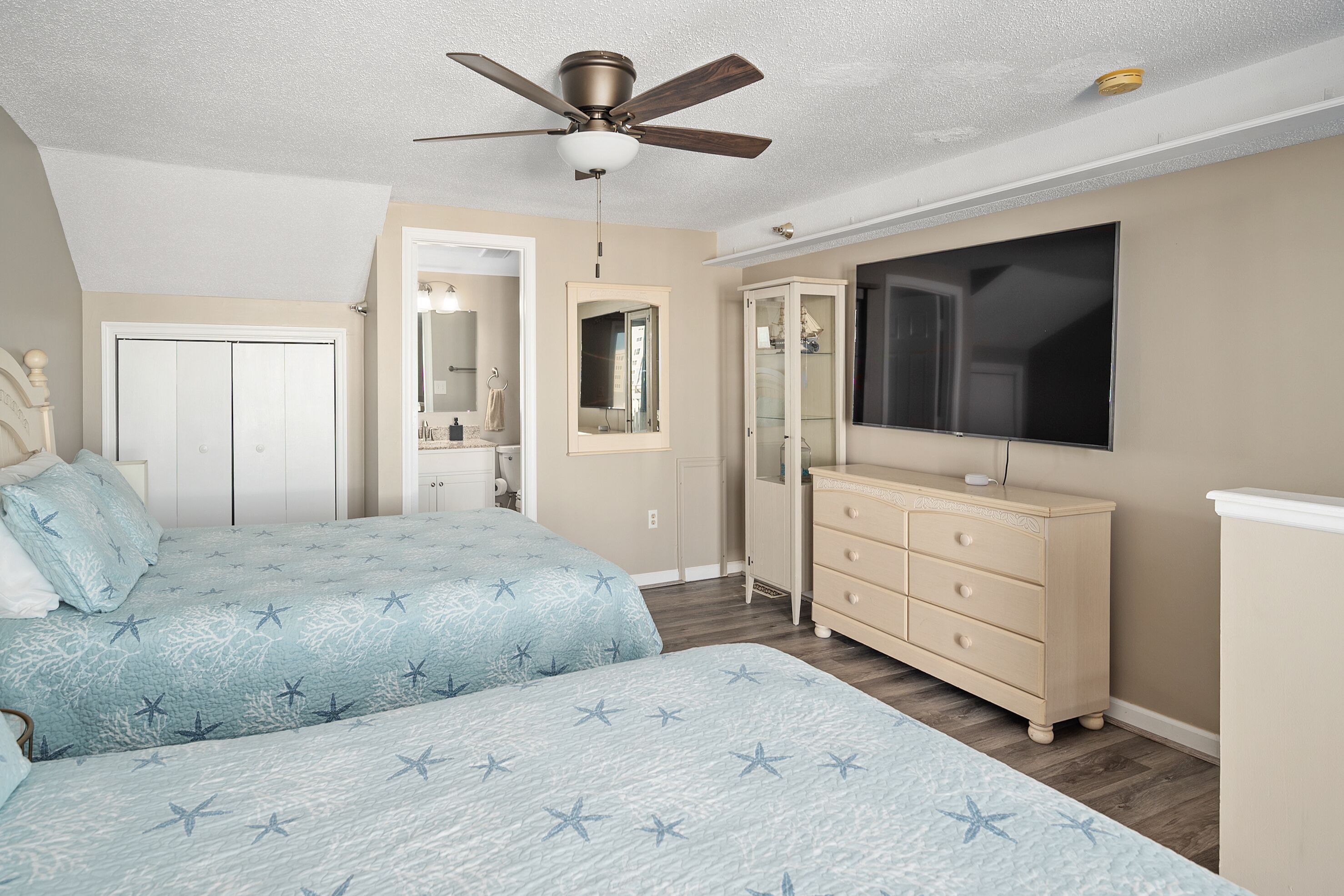 A bedroom with a bed, a dresser, a television, and a ceiling fan.