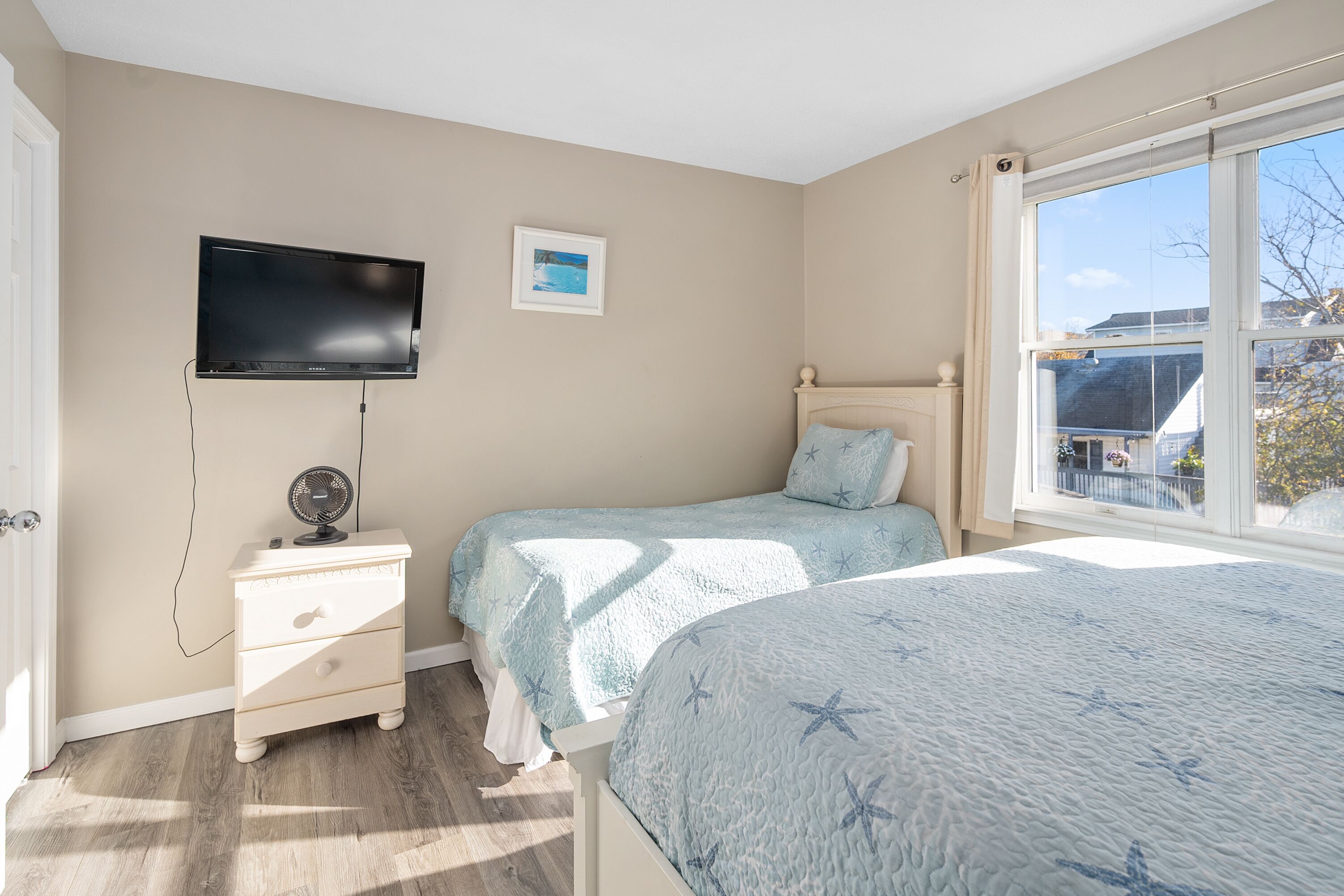 A bedroom with two beds, a TV, a bedside table, and a window with a view.