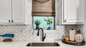 A kitchen with white cabinets, a black faucet, a window with plants, and a tiled backsplash. - Best Lagoon Pool View in Destin • Walk to the Beach • Spacious Stay (Destin)