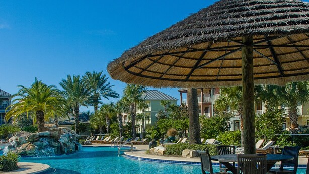 A resort pool area with a thatched umbrella, lounge chairs, and a view of the ocean. - Best Lagoon Pool View in Destin • Walk to the Beach • Spacious Stay (Destin)