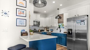 A modern kitchen with white and blue cabinetry, a stainless steel refrigerator, and a central island with bar stools. - Best Lagoon Pool View in Destin • Walk to the Beach • Spacious Stay (Destin)