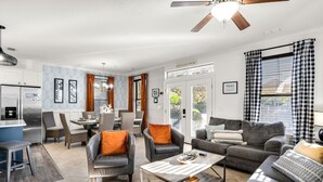 A modern living room with grey sofas, a coffee table, and a dining area with wicker chairs and orange cushions. - Best Lagoon Pool View in Destin • Walk to the Beach • Spacious Stay (Destin)