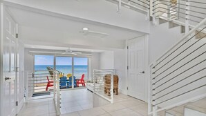 Une pièce spacieuse avec vue sur la mer, un escalier et une porte donnant sur un balcon aménagé avec du mobilier d’extérieur.