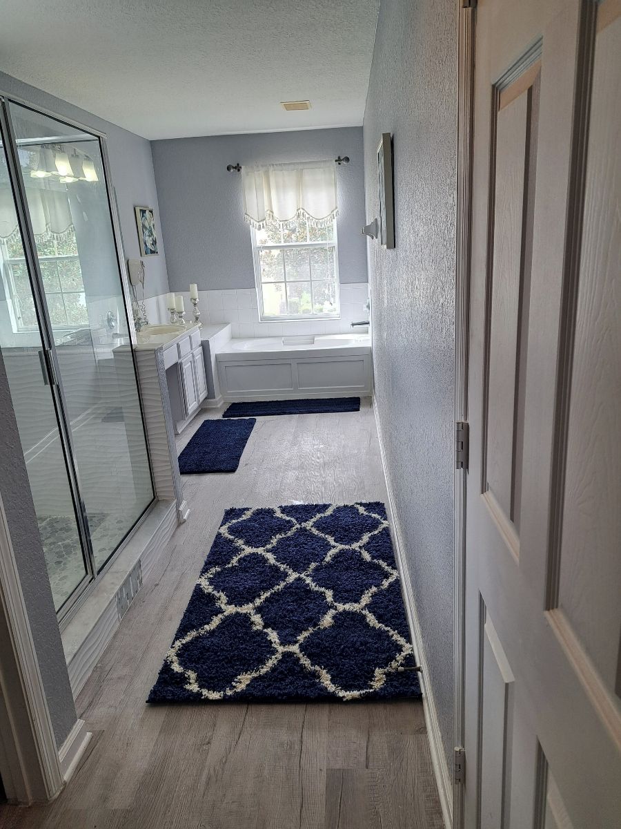 A narrow hallway leading to a bathroom with a window, a sink, and a bathtub.