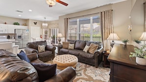 A spacious living room with a large brown leather sofa set, a round ottoman, a wooden coffee table, and a ceiling fan. - Large Windsor Hills Resort pool/Spa Home- Disney (Kissimmee)