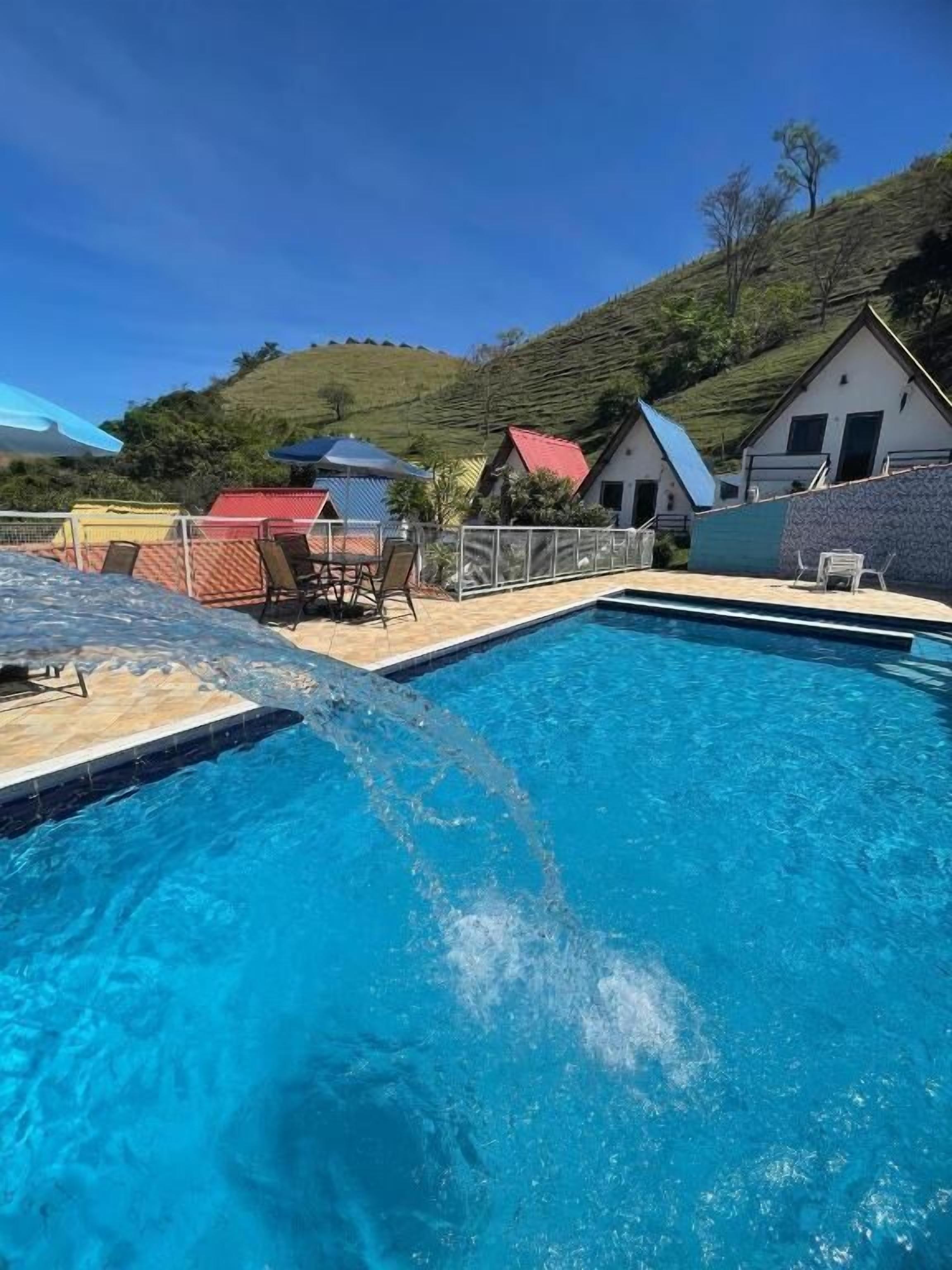 Piscina com água azul cristalina, cercada por área delimitada com cadeiras e guarda-sóis.