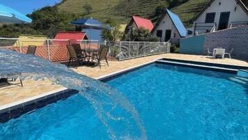 Piscina com água azul cristalina, cercada por área delimitada com cadeiras e guarda-sóis.