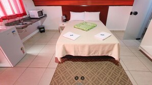 A hotel room with a bed, a microwave, a small refrigerator, a bedside table, and a bathroom door. - Espaço Chalé Cereja (Cachoeira Paulista)