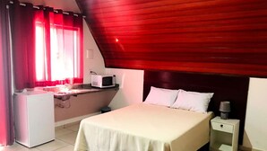 A bedroom with a bed, a nightstand, a microwave, and a small desk. - Espaço Chalé Cereja (Cachoeira Paulista)