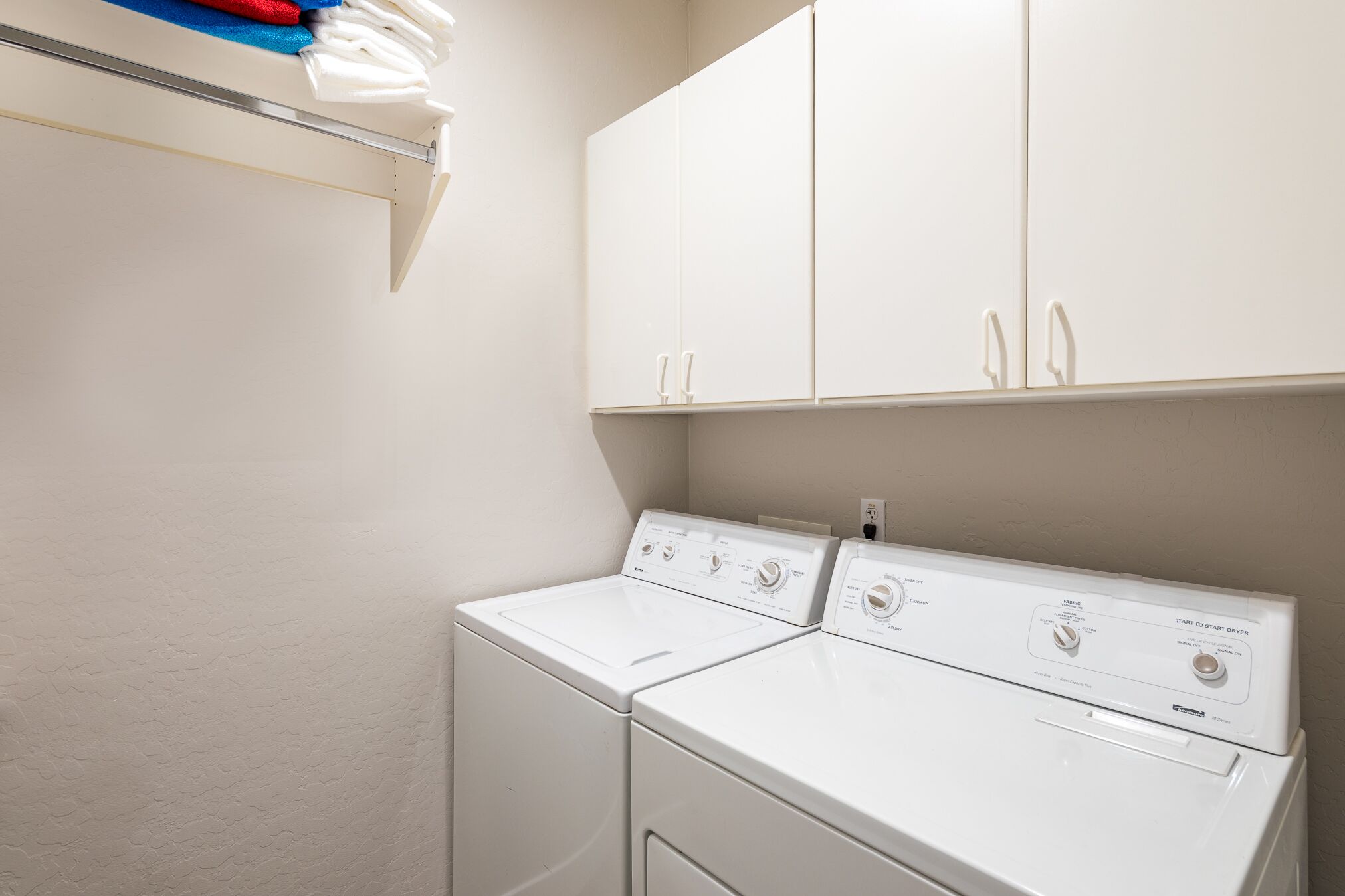 A laundry room with two white front-loading washers and a white cabinet above.