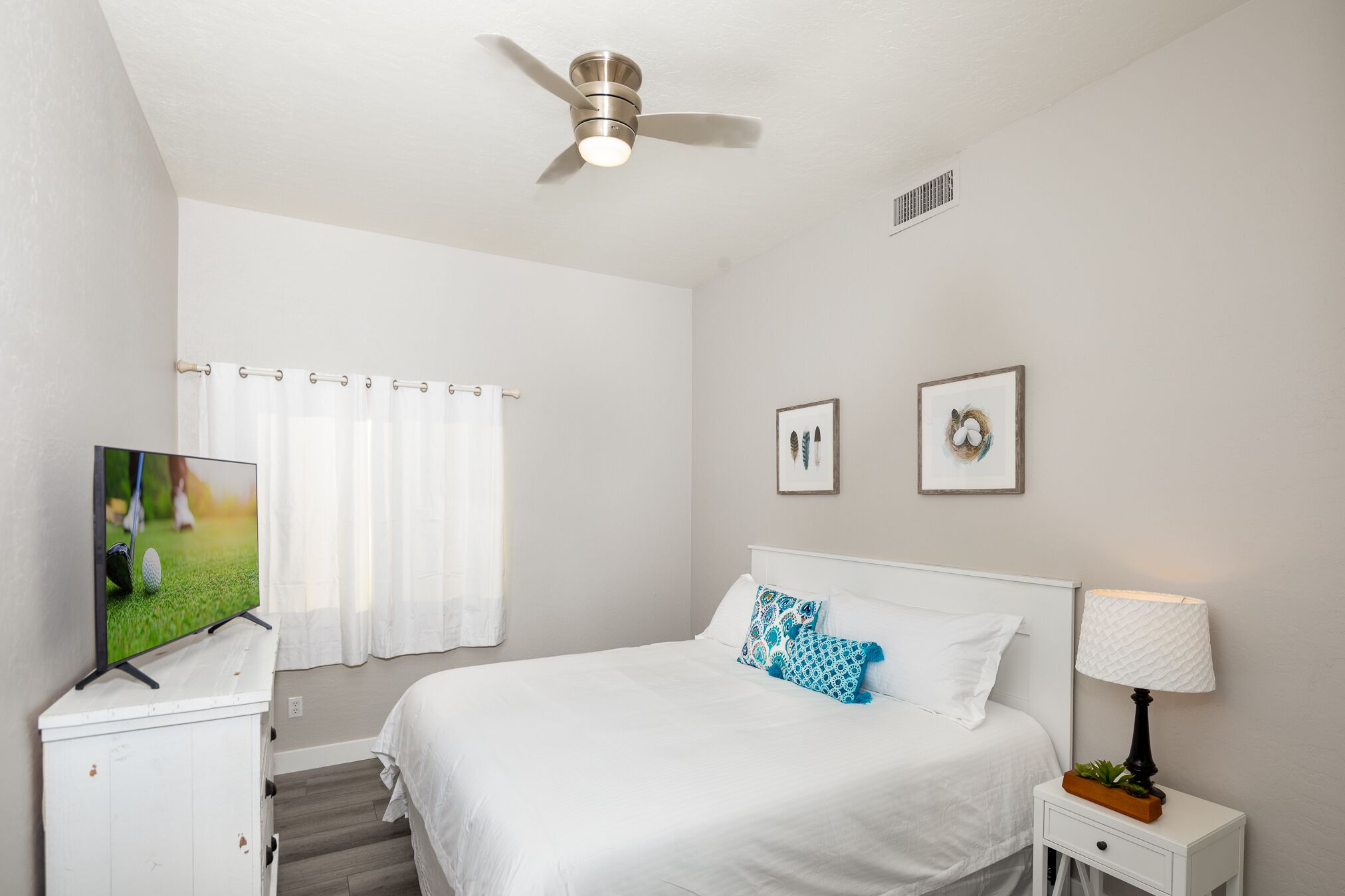A hotel room with a bed, a TV, a ceiling fan, a nightstand, and a window with curtains.