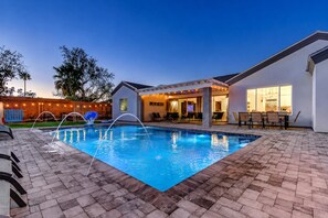 A swimming pool with a patio area, a covered seating area, and a view of the backyard.