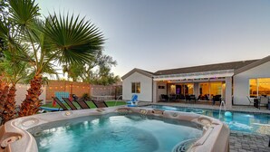A hot tub with a pool, outdoor seating, and a building with a bar area.