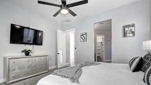 A modern bedroom with a bed, a dresser, a TV, and a ceiling fan.