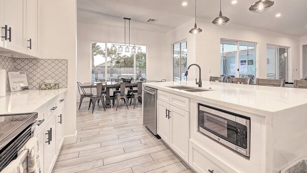 A modern kitchen with white cabinetry, a large island with a sink, a built-in oven, and pendant lighting.