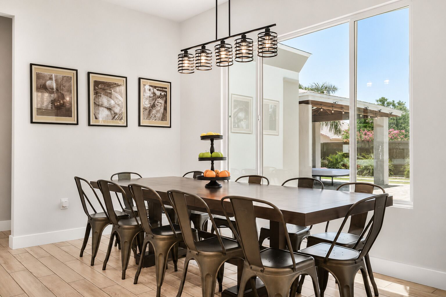 A dining area with a wooden table and chairs, framed artwork on the wall, and a view of the outdoors.