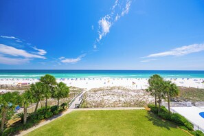 A beach view with a clear sky, a sandy beach, and a grassy area with a pathway leading to the beach.