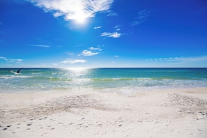 Une plage avec un ciel dégagé, un surfeur dans l’eau et des empreintes de pas sur le sable.
