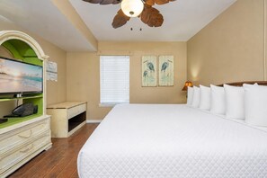 A bedroom with a large bed, a television on a green shelf, a window with blinds, and wall art.