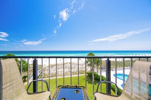 A balcony with two chairs and a pool table, overlooking a beach and ocean.