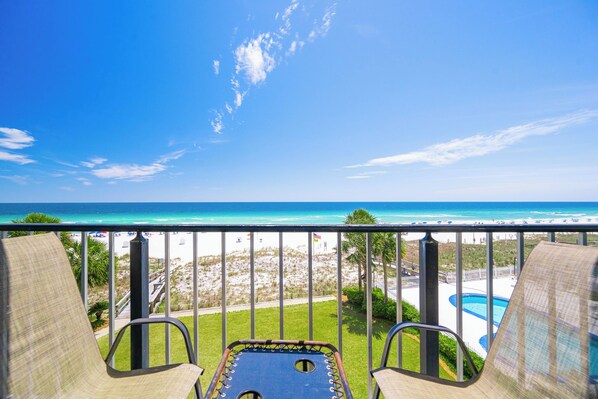 Un balcon avec deux chaises et une table de billard, donnant sur une plage et l’océan.