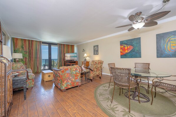 A living room with wicker furniture, a glass-top table, and artwork on the walls.