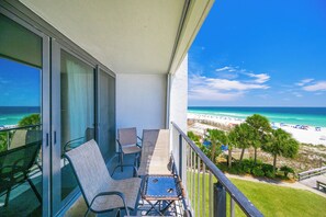 A balcony with a view of a beach, chairs, and a table.