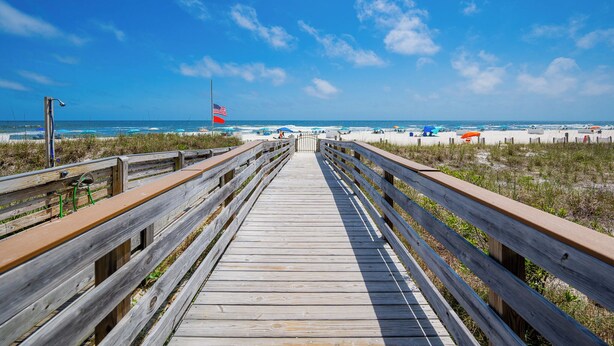 A wooden boardwalk leading to a beach with a flag, sandy dunes, and beach umbrellas. - Beautifully Decorated HOME! ~ Close to EVERYTHING! ~ 2BR 2BA ~ Mariner Lakes (Orange Beach)