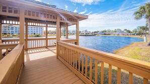 A wooden deck with a view of a water body and buildings in the background. - Beautifully Decorated HOME! ~ Close to EVERYTHING! ~ 2BR 2BA ~ Mariner Lakes (Orange Beach)