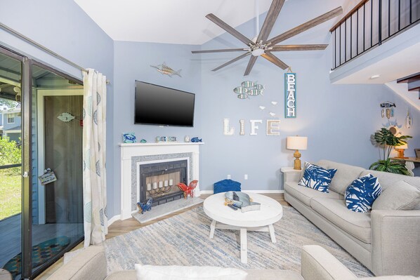 A living room with a fireplace, a ceiling fan, a sofa, and a television.
