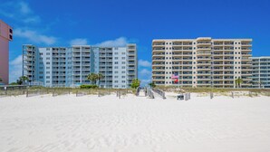 A beachfront hotel with multiple floors, a sandy beach in the foreground, and a clear blue sky. - Beautifully Decorated HOME! ~ Close to EVERYTHING! ~ 2BR 2BA ~ Mariner Lakes (Orange Beach)