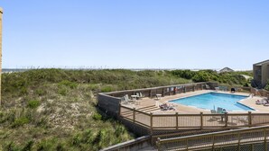 Une terrasse en bois avec une piscine, des chaises longues et une vue sur la plage.