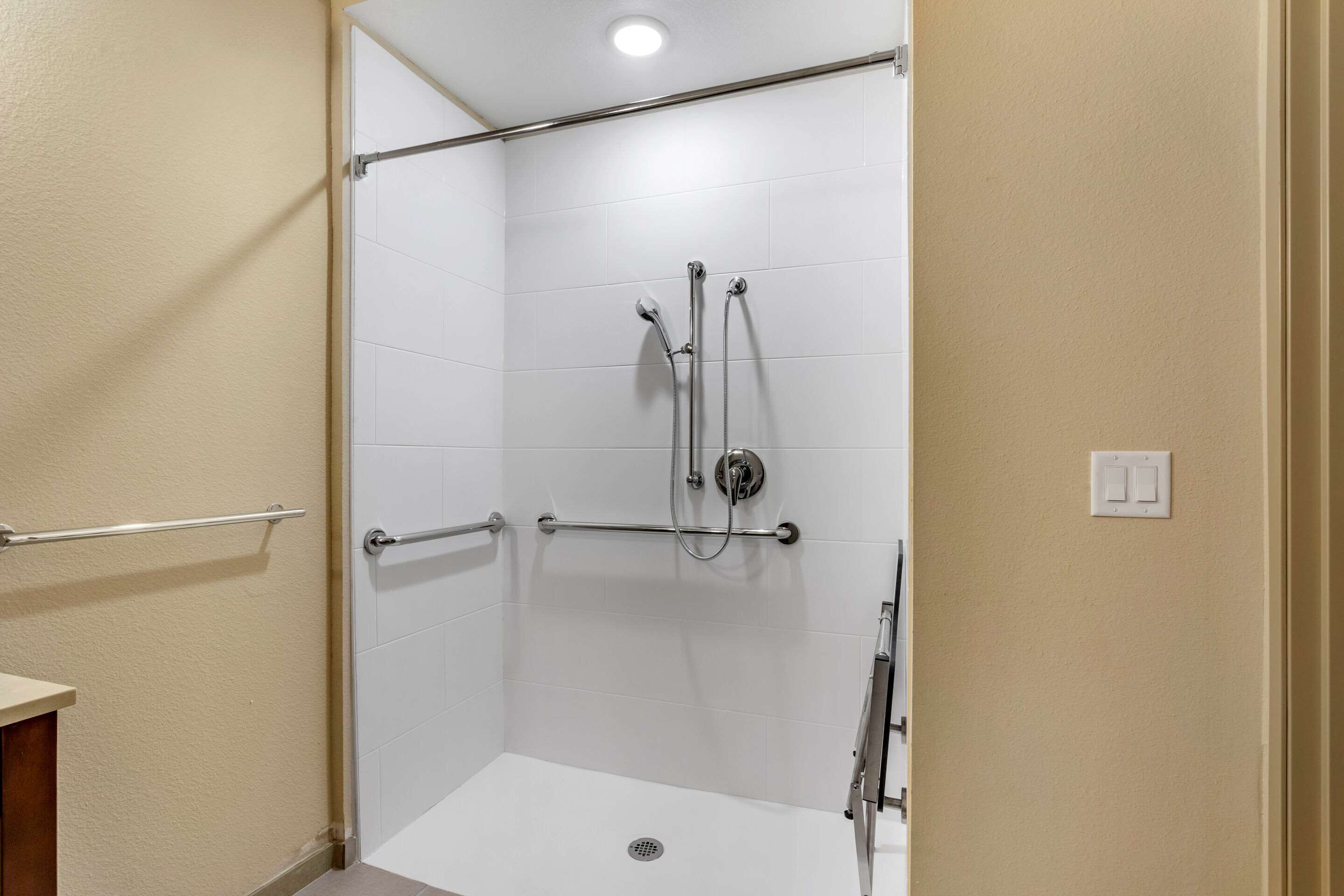 Une douche à l’italienne avec des carreaux blancs, une barre d’appui et un pommeau de douche.