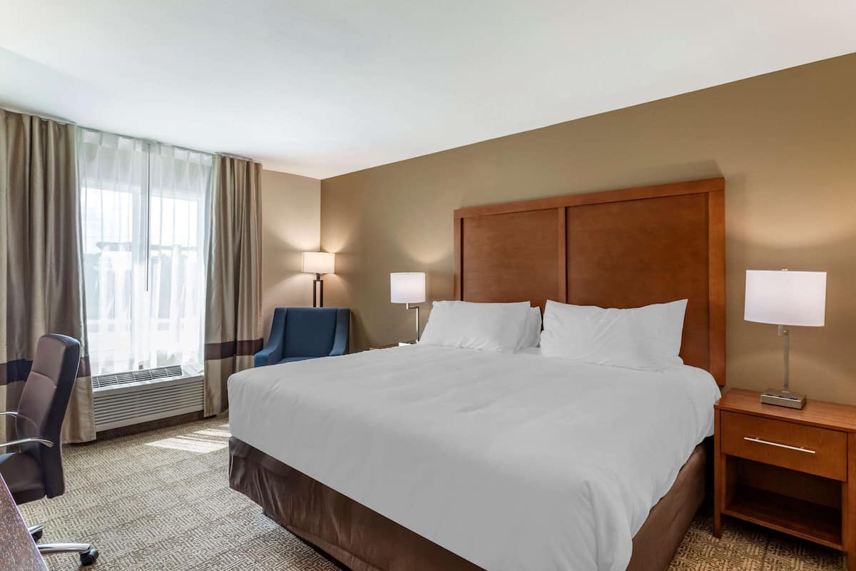 Une chambre d’hôtel avec un grand lit, deux lampes de chevet, un bureau avec une chaise et une fenêtre avec des rideaux.