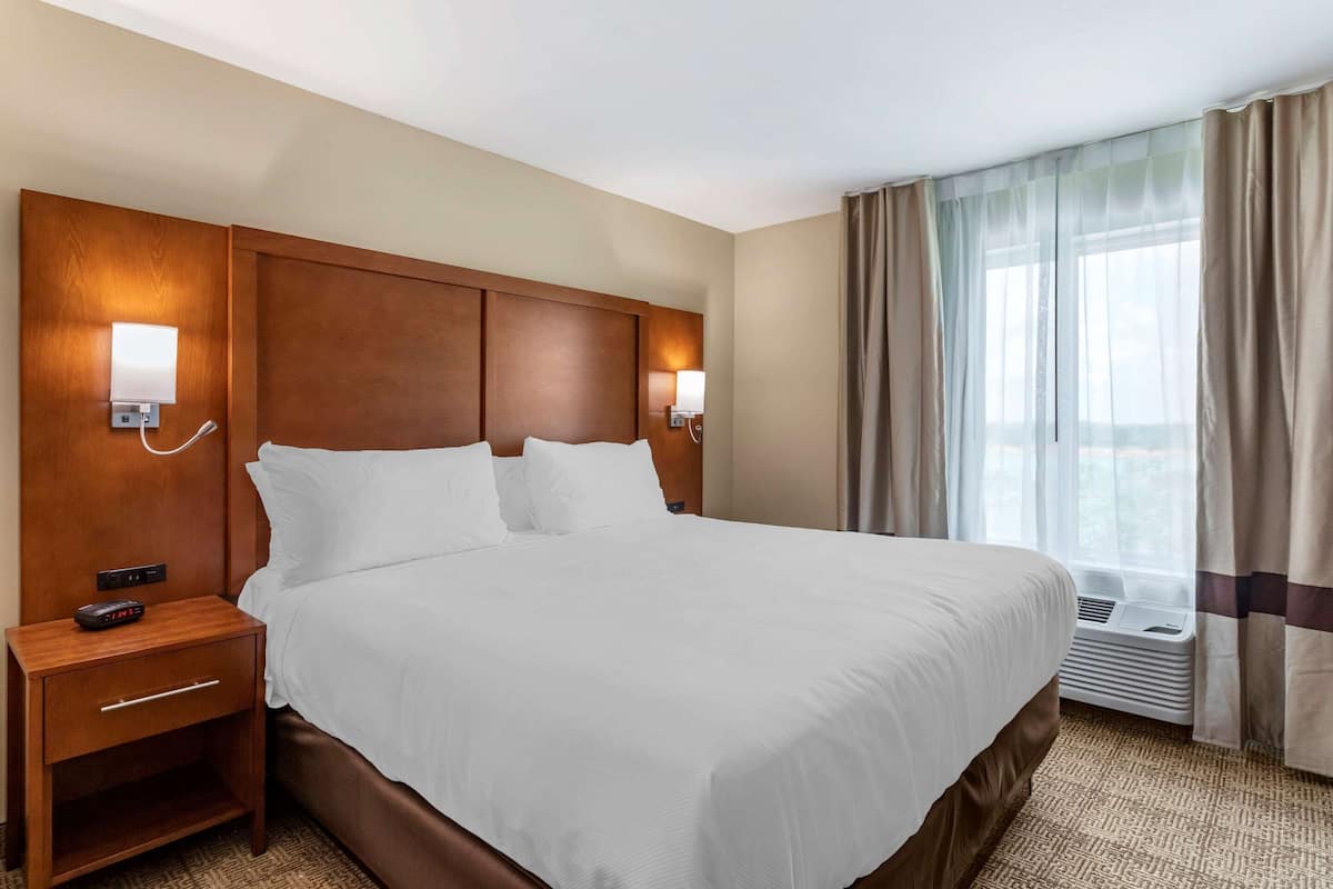 Une chambre d’hôtel avec un grand lit, des tables de chevet avec des lampes, une fenêtre avec des rideaux et un climatiseur fixé au mur.