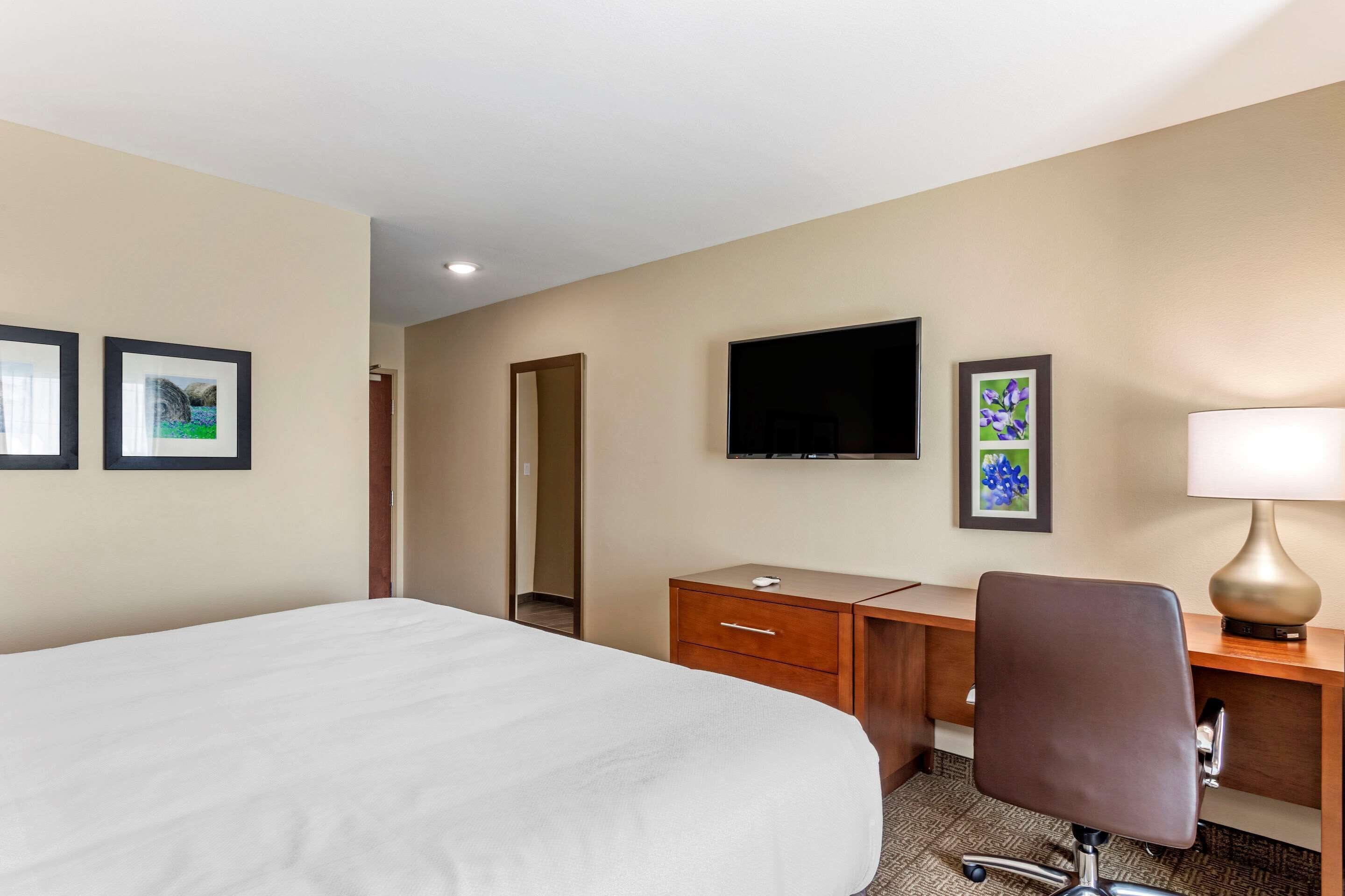 A hotel room with a large bed, a desk with a chair, a flat-screen TV, and framed artwork on the walls.