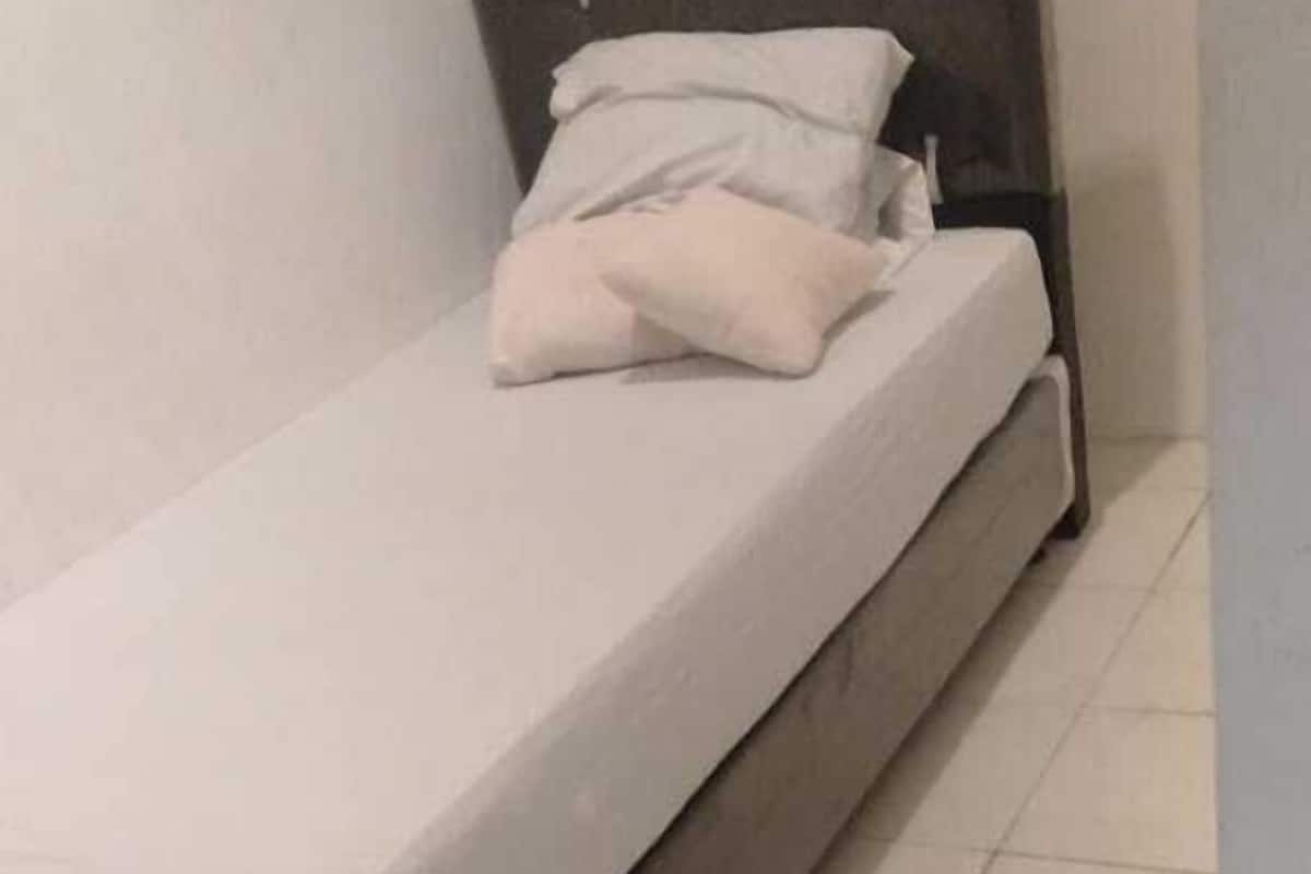 A single bed with a white mattress and pillows, a dark headboard, and a tiled floor.