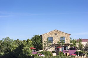 A stone building with a patio area featuring umbrellas and lounge chairs.